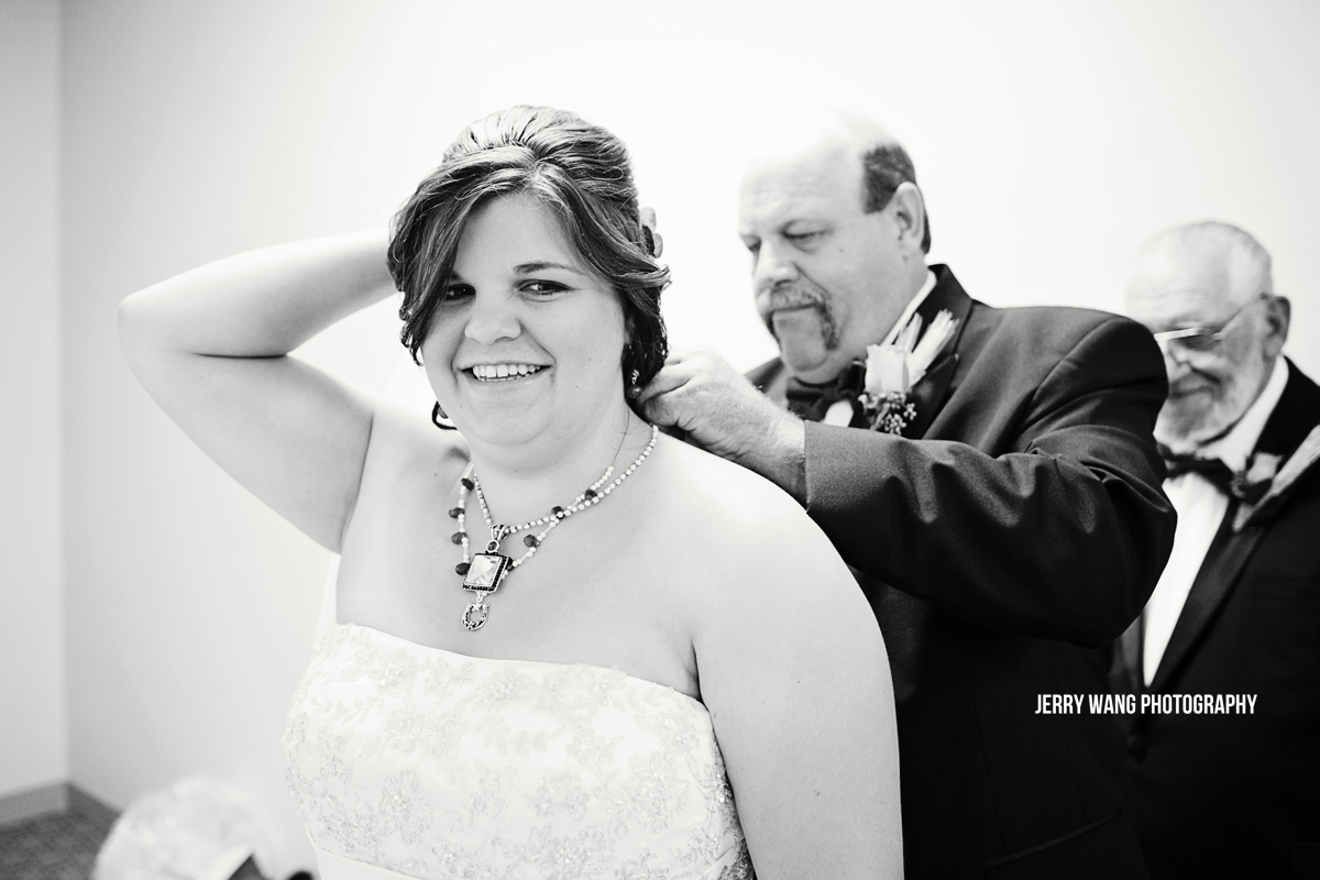The father of the bride putting on a necklace for her.